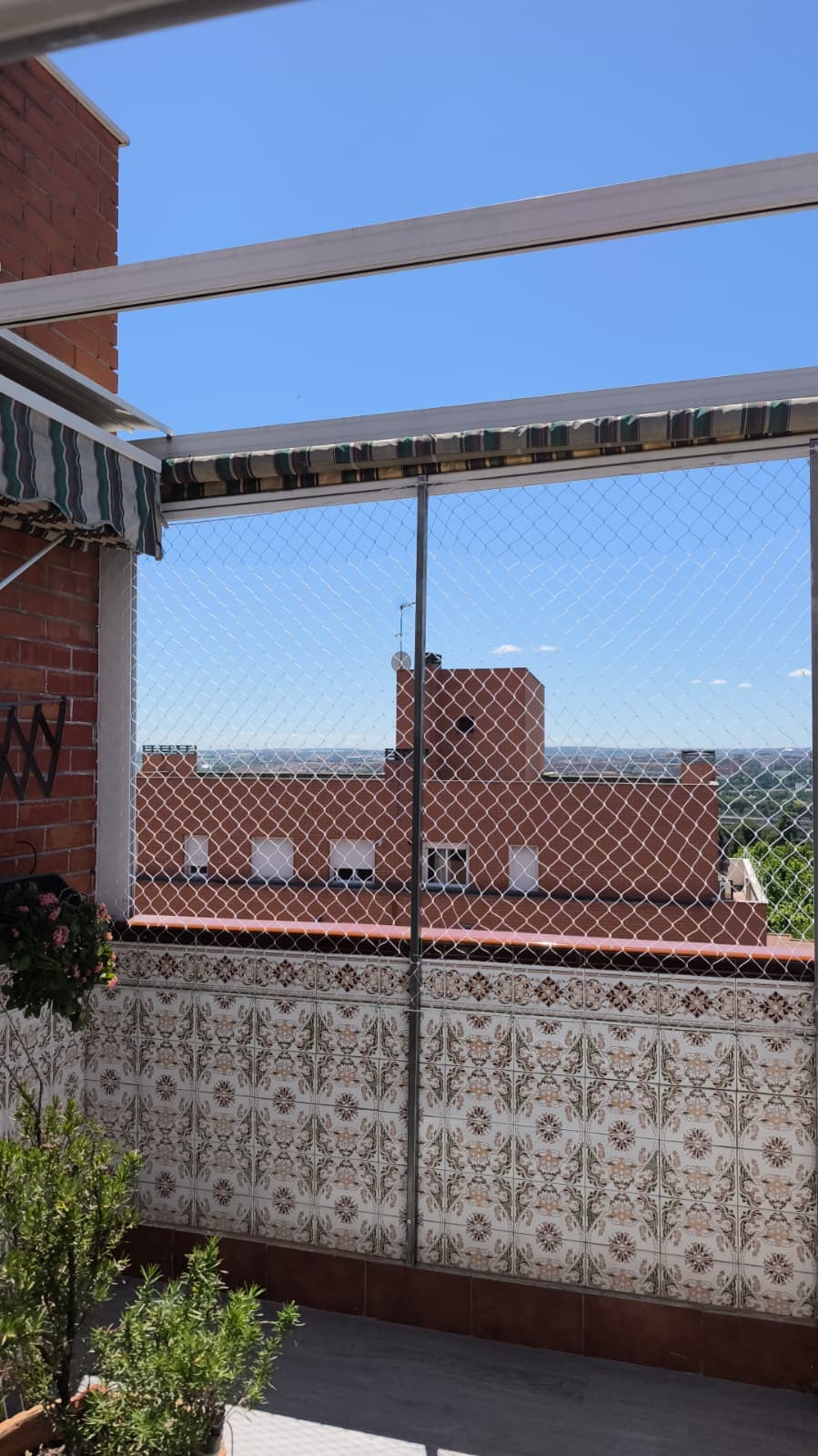 Terraza de un ático en Alcalá de Henares con malla de protección blanca tensada del suelo al techo, con vista a los tejados y al cielo