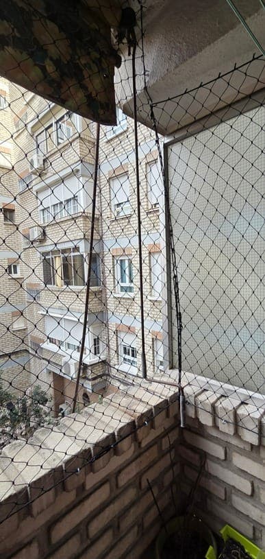 Balcón de una vivienda con red de protección blanca instalada de la barandilla al techo