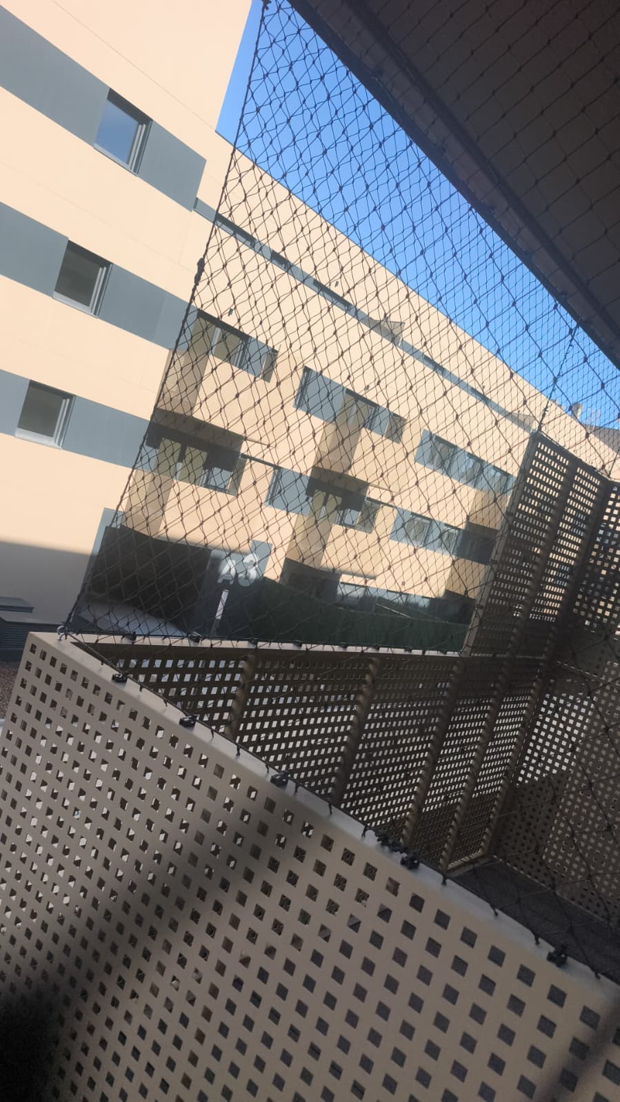 Malla de protección en un balcón, con el bloque de enfrente al fondo