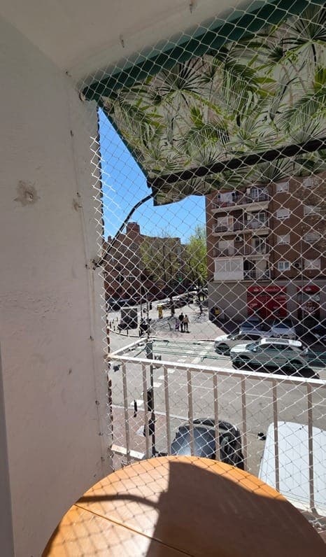 Vista desde dentro de un balcón protegido con malla, mirando a la calle y a los coches aparcados