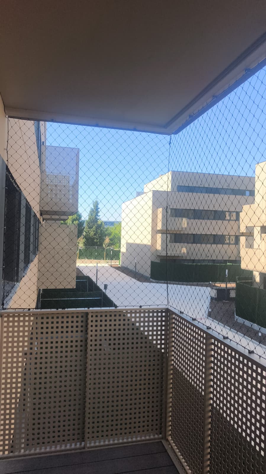 Balcón con celosía y malla de protección, con vista a los bloques del barrio